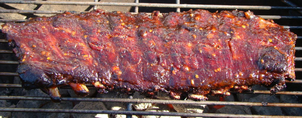 Glazed barbecue ribs cooking on charcoal grill